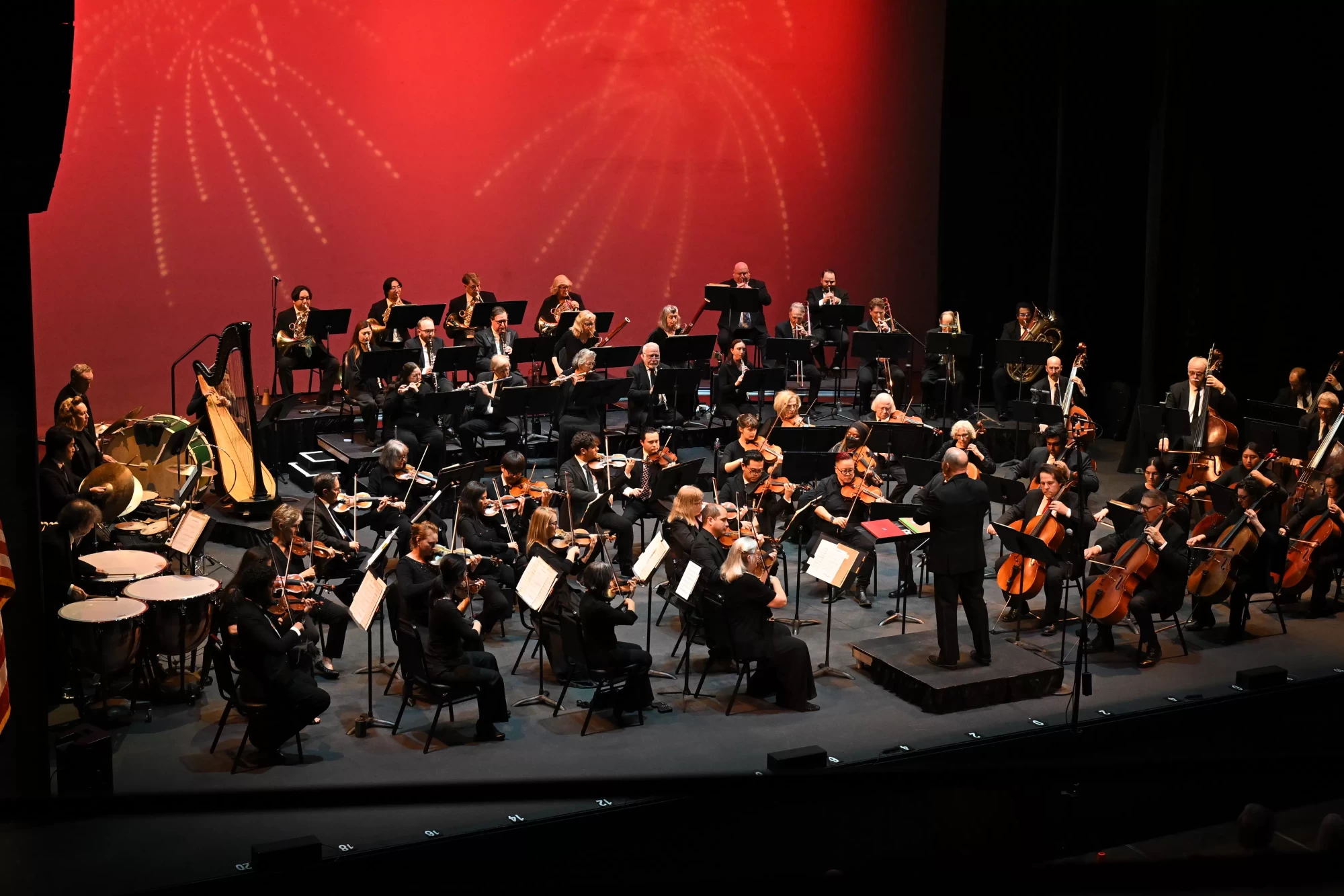 The La Mirada Symphony performing on stage under red lights as the conductor leads the orchestra