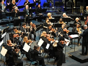 Symphony orchestra performing on a concert stage as the conductor leads from the podium
