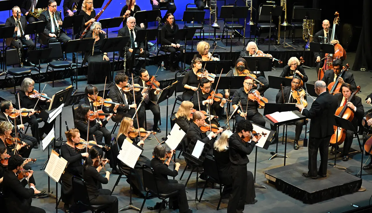 Symphony orchestra performing on a concert stage as the conductor leads from the podium