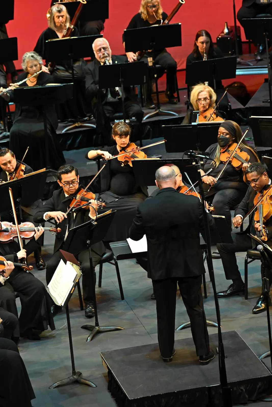 Conductor leading La Mirada Symphony violinists from the podium, with the woodwind section playing behind them during a live concert