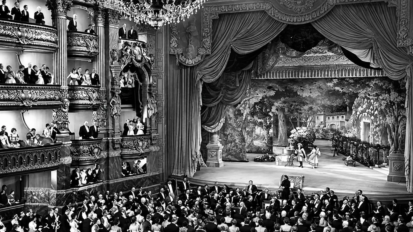 Black-and-white recreation of the grand Paris Opera House interior from The Phantom of the Opera (1925), showing ornate balconies, a theatrical stage and a crowded audience.
